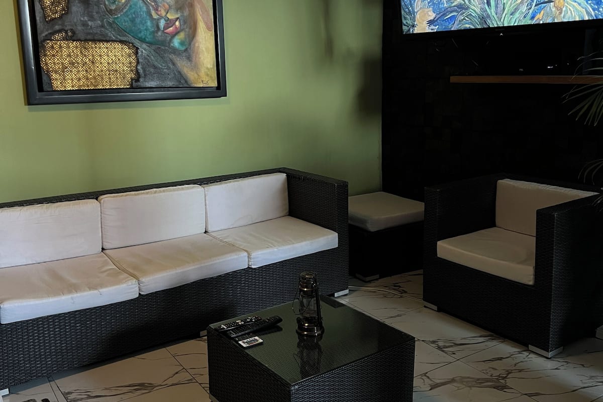 A living room with a sofa, two armchairs, a coffee table, a painting, and a TV.