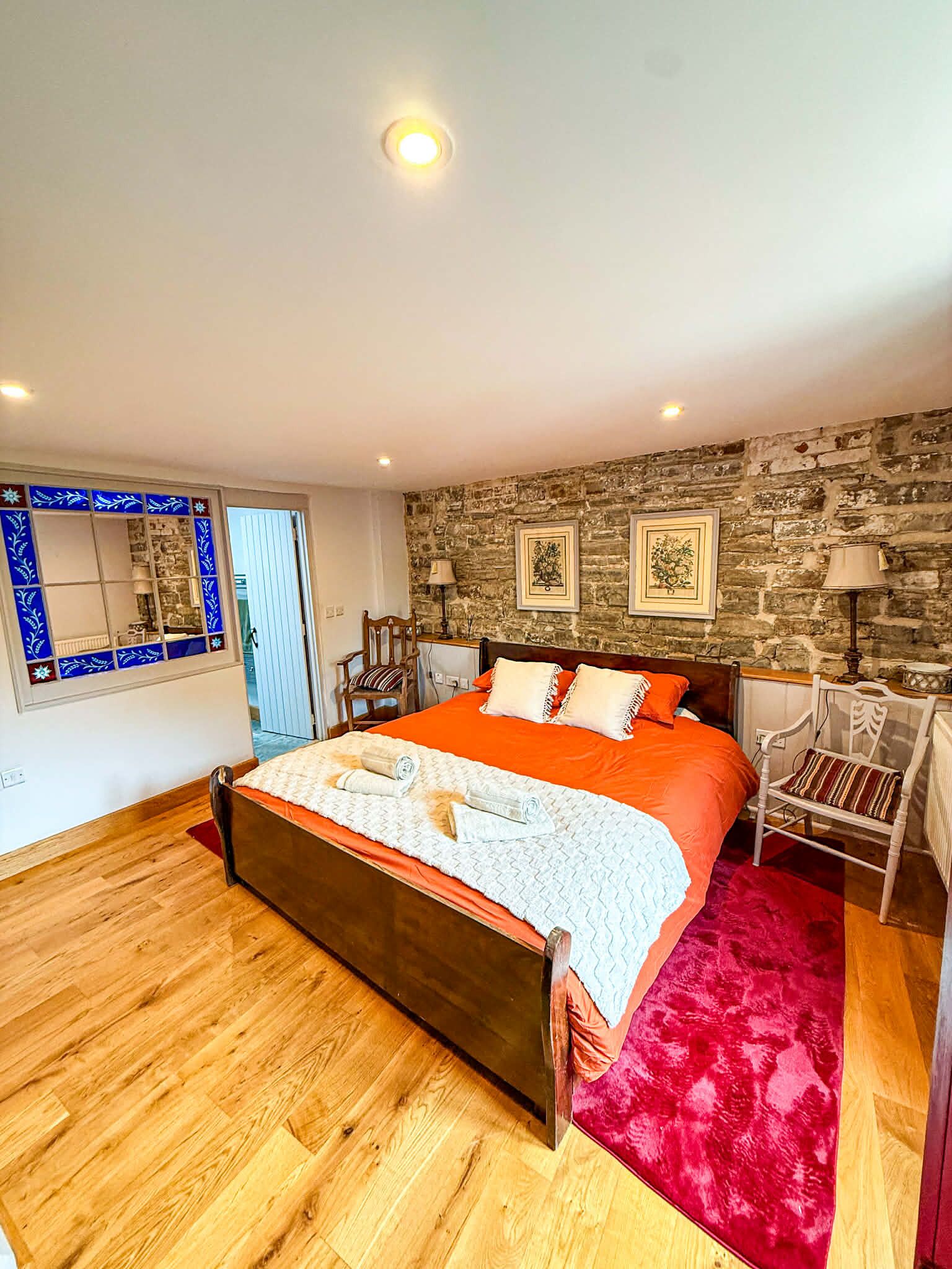 Un dormitorio con cama de madera, pared de piedra y ventana con paneles decorativos azules.