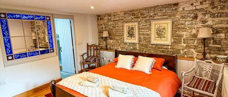 Un dormitorio con cama de madera, pared de piedra y ventana con paneles decorativos azules.