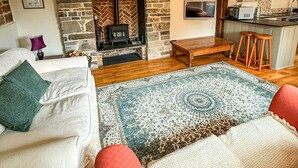 A cozy living room with a fireplace, a sofa, a coffee table, and a kitchen area with a bar stool.