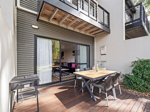 Eine moderne Außenpatio mit Holztisch und -stühlen, einer Schiebetür zu einem Innenbereich und einem kleinen Außenbereich mit einer Bank.
