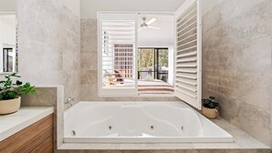Une salle de bain moderne avec une grande baignoire, une fenêtre avec des stores et une vue sur un balcon.