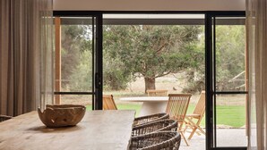 A dining area with a wooden table, wicker chairs, and a view of the outdoors through large glass doors.