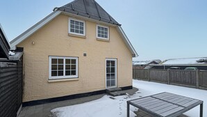 Ein zweistöckiges Haus mit beiger Fassade, grauem Dach und einem Holzzaun im Hintergrund.