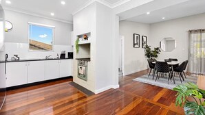 A modern kitchen with white cabinets, a built-in oven, and a dining area with a round table and chairs. - Sasha's Cottage on the Hill | BBQ & Entertainment (Perth)