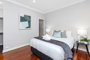 A modern hotel room with a large bed, bedside lamps, a framed abstract artwork, and a small side table with a plant.