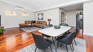 A modern living room with a sofa, coffee table, and dining table with chairs. - Sasha's Cottage on the Hill | BBQ & Entertainment (Perth)