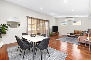 A modern living room with a dining area, a flat-screen TV, and a sofa set.