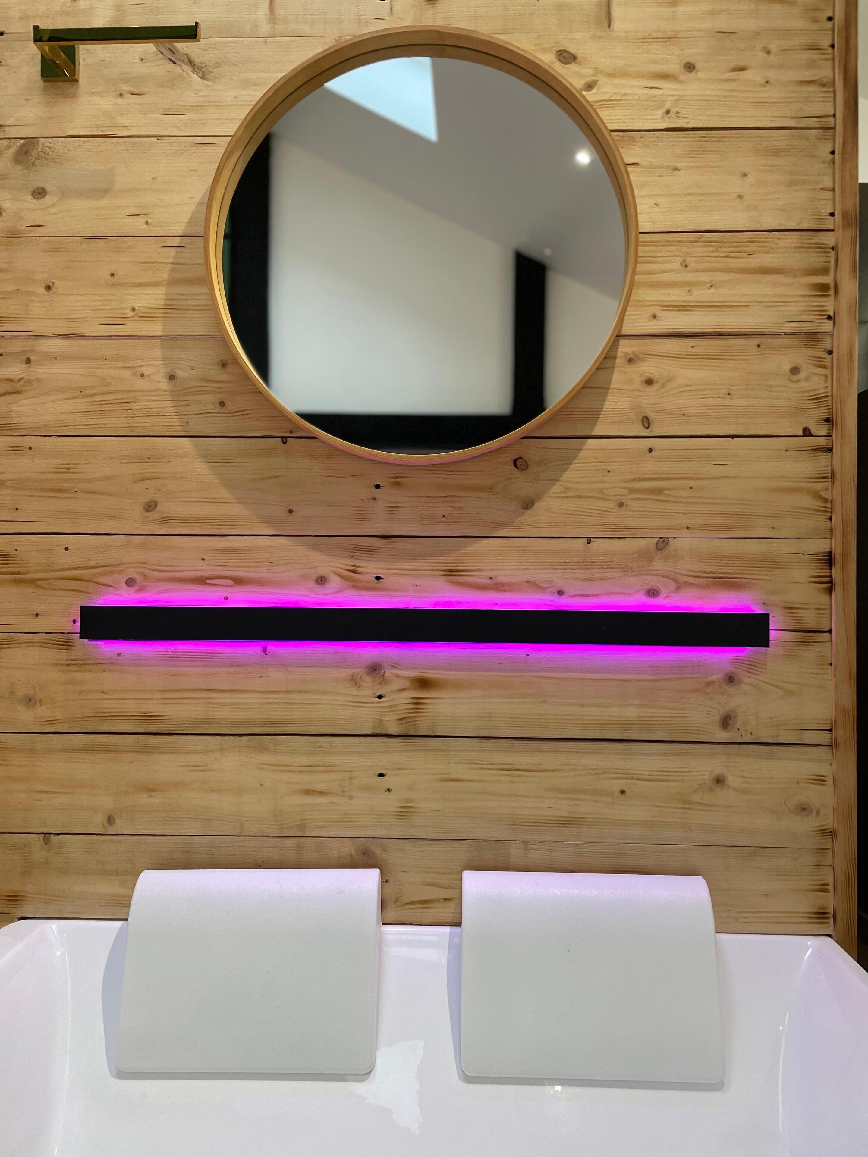 A wooden wall with a round mirror and a white sink with two towel dispensers.