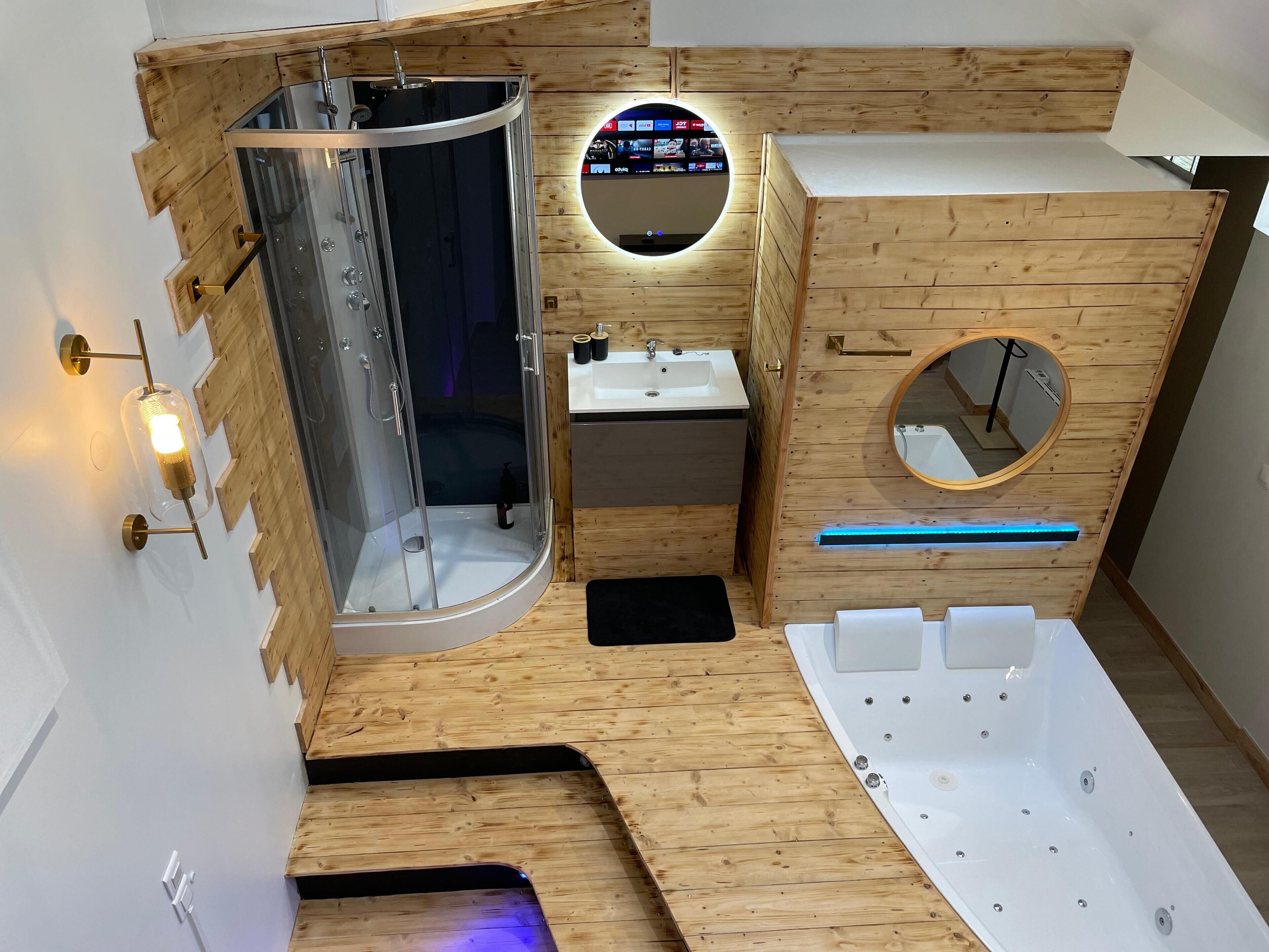 A modern bathroom with a glass-enclosed shower, a vanity with a mirror, a bathtub, and a wooden floor.