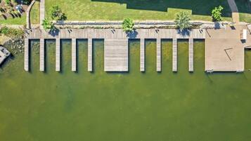 An aerial view of a dock extending into a body of water, surrounded by greenery and a paved walkway.