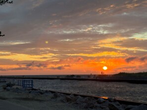 Ein Sonnenuntergang über einem Gewässer mit felsiger Uferlinie und einem Holzsteg.