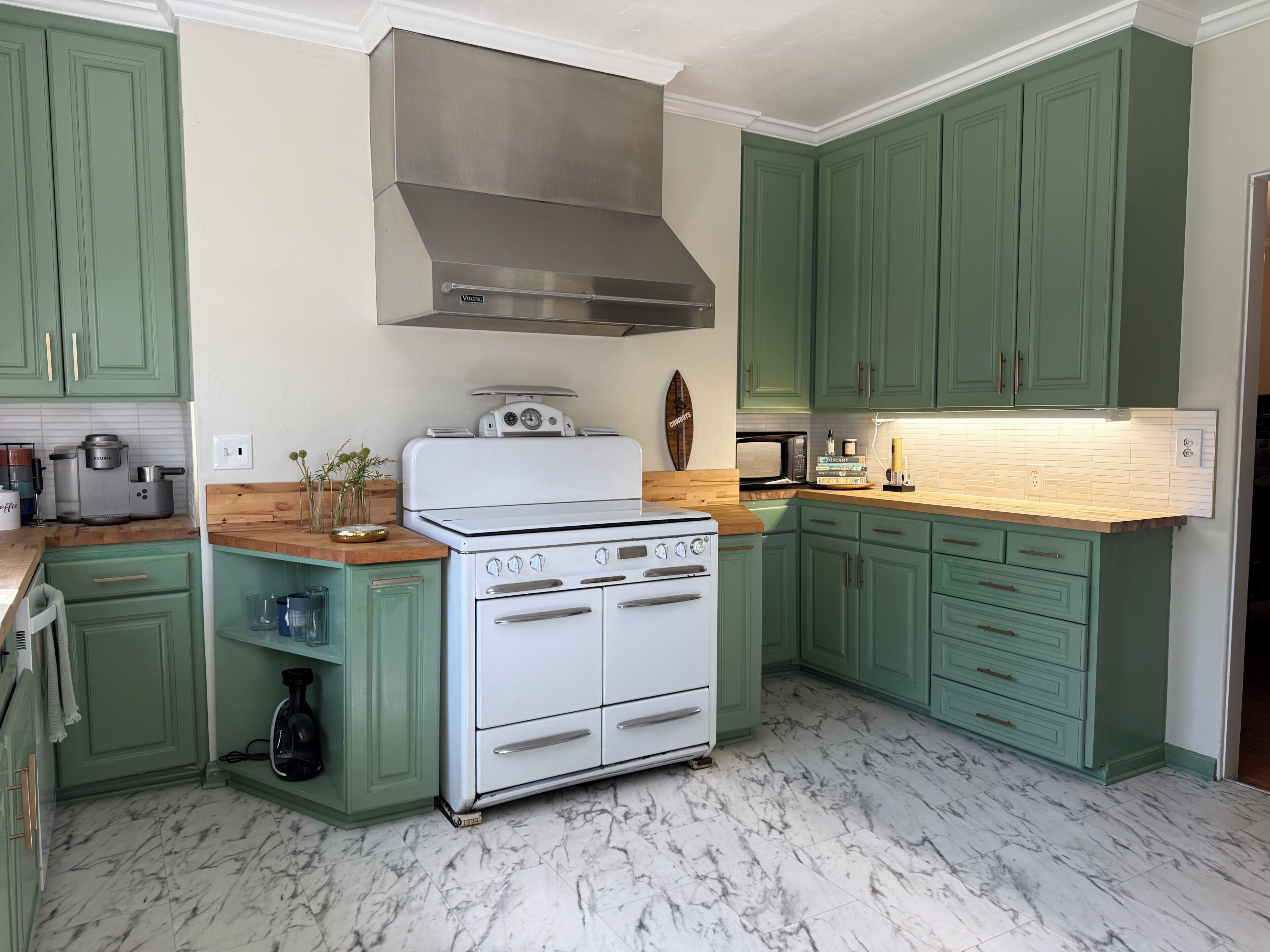A kitchen with green cabinets, a white stove, and a stainless steel range hood.