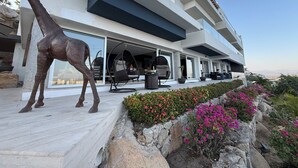 A modern building with a large sculpture of a giraffe, outdoor seating, and a stone retaining wall with flowering plants. - Luxury villa with ocean view and private pool. Expectacular | 10 guests (Acapulco de Juárez)