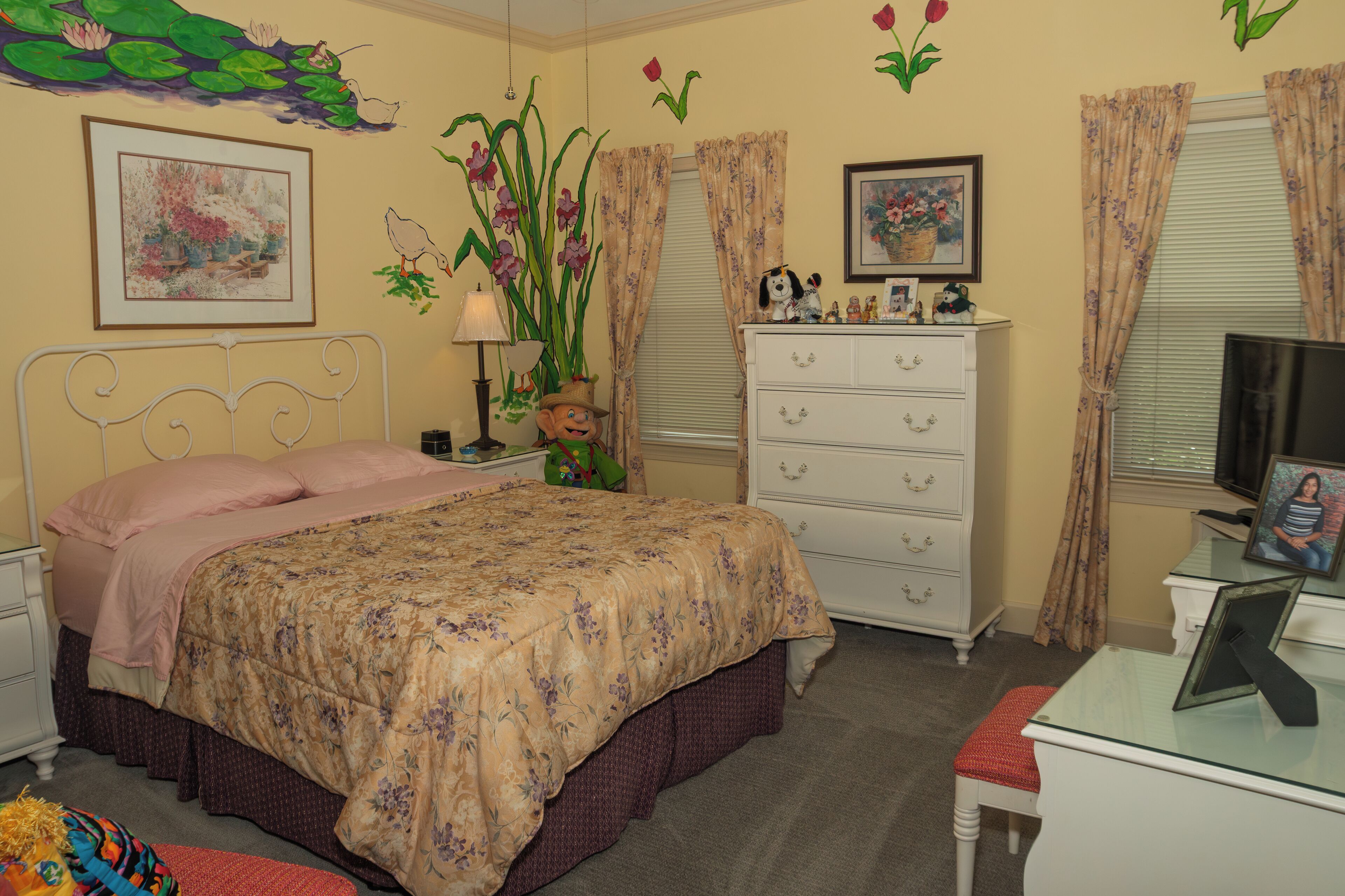 A bedroom with a bed, dresser, desk, and a television.