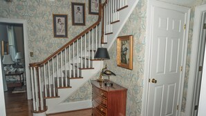 Una escalera de madera con barandilla blanca, un aparador de madera con cajones, una puerta con picaporte de latón y papel tapiz estampado.