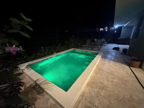 A rectangular pool with a green light, surrounded by a concrete deck, with chairs and a table in the background. - Private Tropical Villa in Marbella, Modern Comfort Just Minutes from the Beach! (Provincia de Guanacaste)