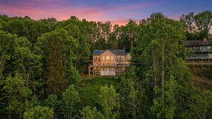 Ein zweistöckiges Haus, umgeben von dichtem Wald, mit Balkon und mehreren Fenstern.