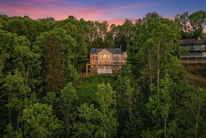 Ein zweistöckiges Haus, umgeben von dichtem Wald, mit Balkon und mehreren Fenstern.