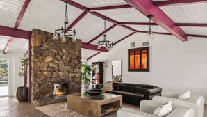 Ein geräumiges Wohnzimmer mit Kamin aus Stein, einem schwarzen Ledersofa, einem weißen Sofa und einem Glastisch.