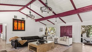 Ein geräumiges Wohnzimmer mit einer schwarzen Ledersofa, einem weißen Sessel, einem Glastisch und einem großen abstrakten Gemälde an der Wand.