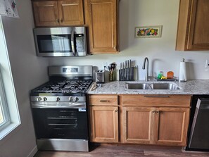 A kitchen with stainless steel appliances, wooden cabinets, a marble countertop, and a sink. - Cozy 1-bedroom apartment in Grand Island located on an urban farm. (Grand Island)