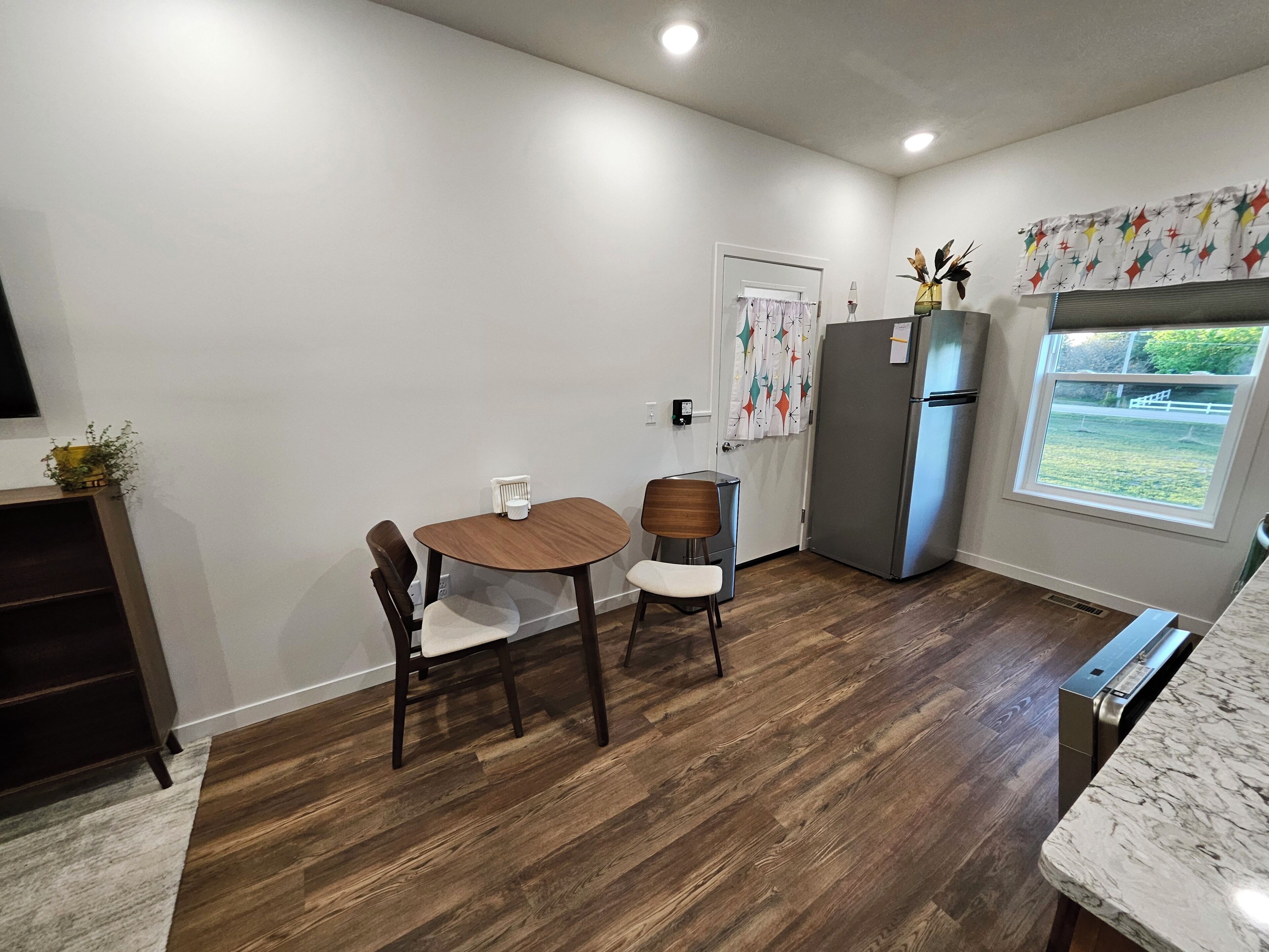 A compact kitchen with a dining table, chairs, a refrigerator, and a window with a view.