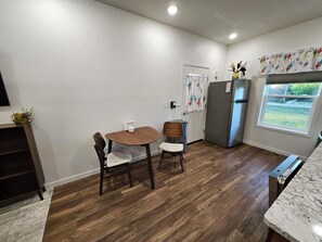 A compact kitchen with a dining table, chairs, a refrigerator, and a window with a view. - Cozy 1-bedroom apartment in Grand Island located on an urban farm. (Grand Island)