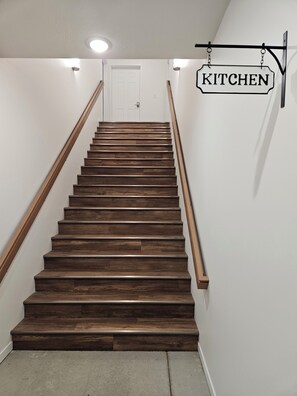 Eine Holztreppe mit einem 'KÜCHE'-Schild darüber, das zu einer weißen Tür führt.