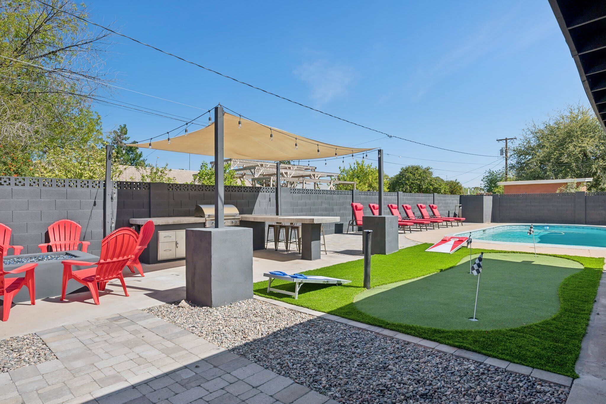 An outdoor patio with a barbecue grill, red chairs, a pool table, and a small putting green.