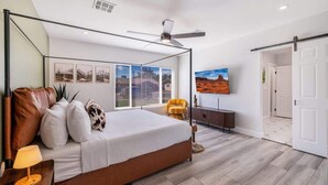 A bedroom with a four-poster bed, a ceiling fan, a TV mounted on the wall, and a door leading to another room. - Casa Mesa • Private Paradise w Pool, Putt, & Games (Mesa)