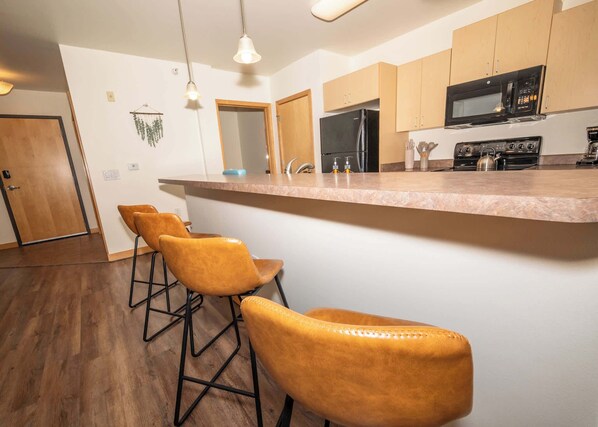 A kitchen with a central island, bar stools, wooden cabinets, a microwave, and a refrigerator.