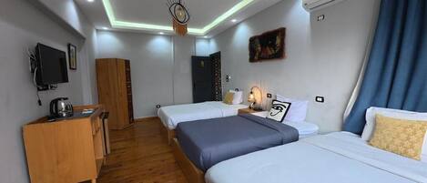 Una habitación de hotel con dos camas, un escritorio con hervidor, televisión y lámpara en el techo.