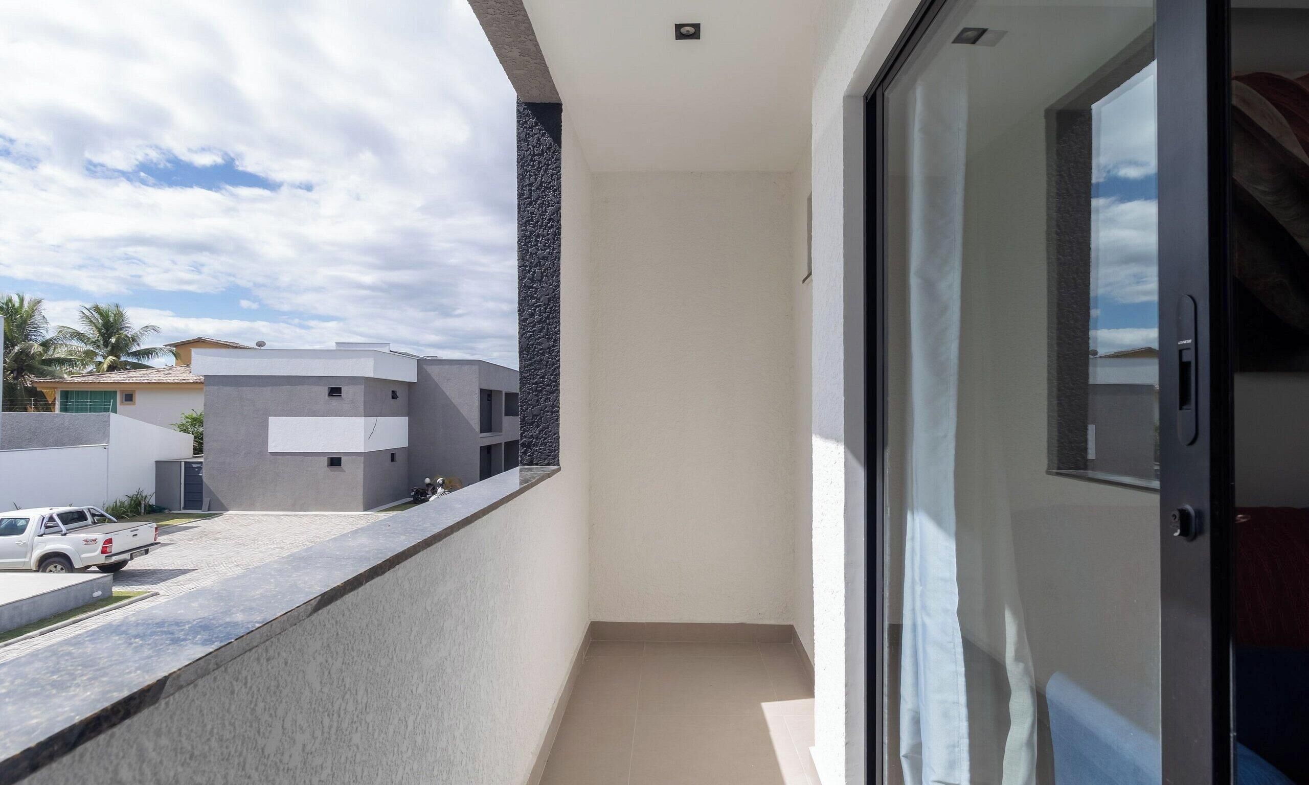 En balkon med udsigt til en moderne bygning, en parkeret bil og en klar himmel.