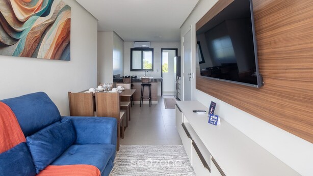 A modern living room with a sofa, a flat-screen TV mounted on the wall, a dining area with a kitchen in the background, and a large abstract painting on the wall. - Modern Apartment in a Condo With Pool Rnm0015 (Porto Seguro)