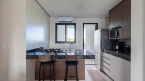 A modern kitchen with a central island, two bar stools, a built-in microwave, and a refrigerator. - Modern Apartment in a Condo With Pool Rnm0015 (Porto Seguro)