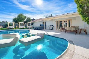 A swimming pool with lounge chairs, a covered patio area, and a building with large windows. - LUX 6BR/3BA Stylish House w/Pool & Jacuzzi (Las Vegas)