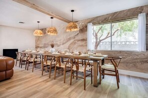 A dining area with a long wooden table, matching chairs, and pendant lights. - LUX 6BR/3BA Stylish House w/Pool & Jacuzzi (Las Vegas)