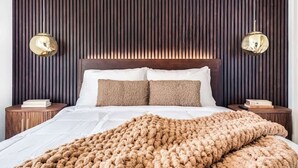 Ein Schlafzimmer mit einer Wand aus Holzlatten, einem großen Bett mit weißer Bettwäsche, zwei Nachttischen und zwei Wandlampen.