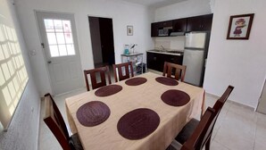Een eetgedeelte met een tafel voor zes personen, omringd door stoelen, in een kamer met een keuken op de achtergrond.
