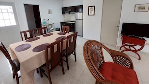 Een eetgedeelte met een tafel, stoelen, een televisie en een keuken op de achtergrond.