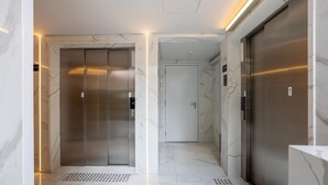 A modern elevator area with marble walls, a metal elevator door, and a lit pathway. - Condo. w/ Rooftop Pool, 270m fr/ the Metro, Jardins - Gabs (São Paulo)
