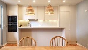 Una cocina moderna con armarios blancos, horno empotrado y una zona de comedor con dos sillas de madera.