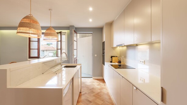 Una cocina moderna con una isla central, luces colgantes y vistas al exterior.