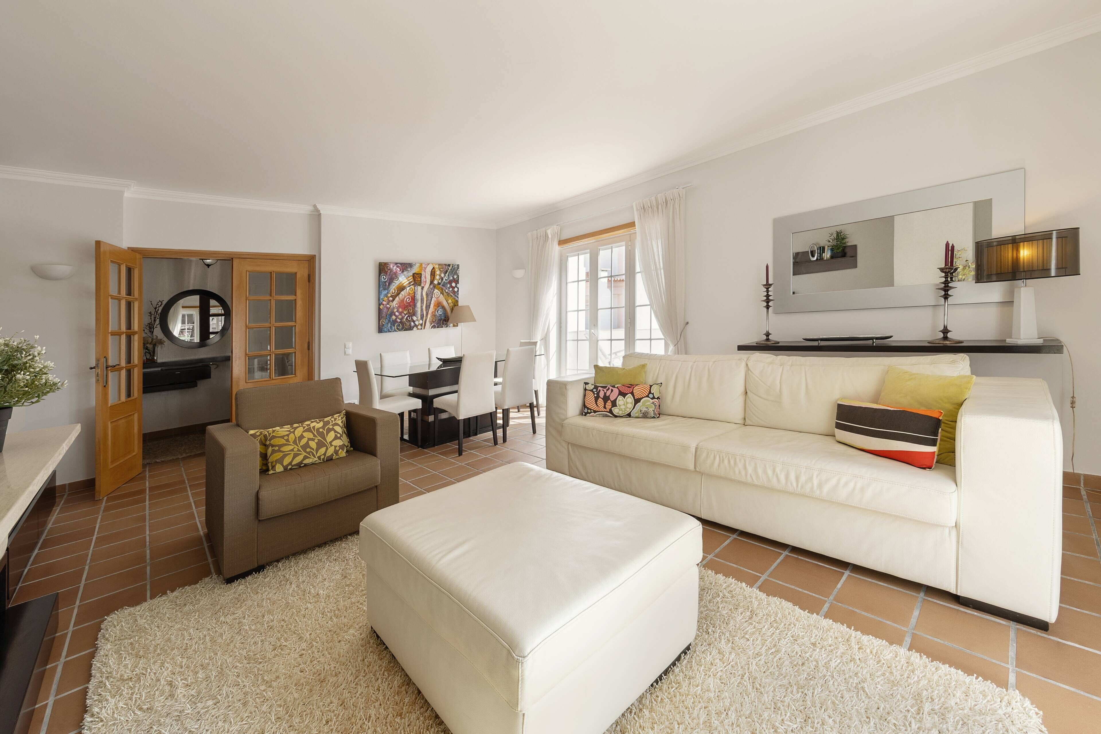 Un salon comprenant un canapé, un pouf et un coin repas avec des chaises et une table.