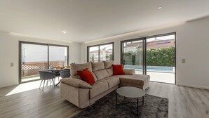 A modern living room with a sofa, coffee table, and a view of a swimming pool. - Quinta Atia – Private Pool Hideaway (Caldas da Rainha)