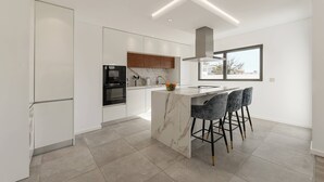 A modern kitchen with a marble island, bar stools, and a large window. - Quinta Atia – Private Pool Hideaway (Caldas da Rainha)
