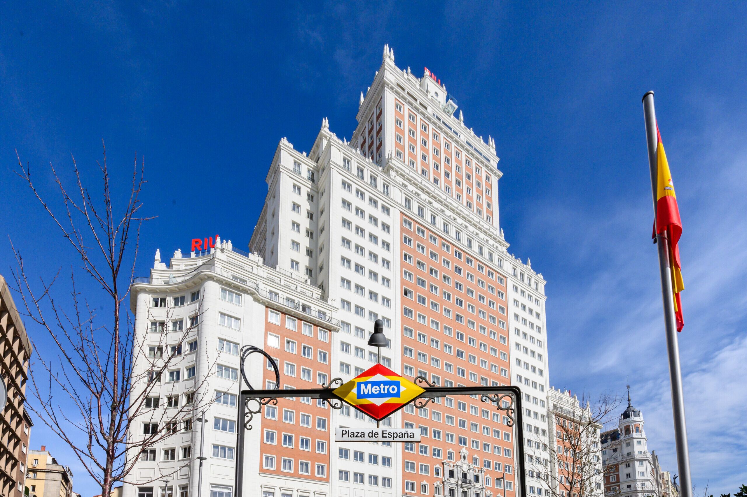 A multi-story building with a Metro sign, Plaza de España, and a flag.