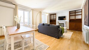 Ein Wohnzimmer mit einer Couch, einem Esstisch mit Stühlen, einem an der Wand befestigten Fernseher und einem Kamin.