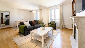 Ein Wohnzimmer mit weißem Couchtisch, einer Couch, einem Sessel, einem Kamin und einem großen Fenster.